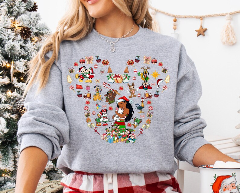 A woman wearing a gray sweatshirt with a heart-shaped design featuring various Disney characters and holiday-themed elements.