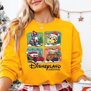 A woman wearing a yellow sweater with a Disney-themed graphic on it, including characters from the Disney movie Cars.