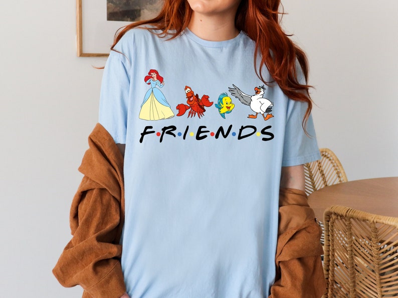K&ouml;nnte beinhalten: Hellblaues T-Shirt mit einem Aufdruck von Arielle, Sebastian, Flounder und Scuttle aus Arielle, die Meerjungfrau. Der Aufdruck ist im Stil des Friends-Logos und lautet "FRIENDS".