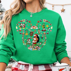 A woman wearing a green sweater with a large, colorful design of various Disney characters and holiday-themed elements.