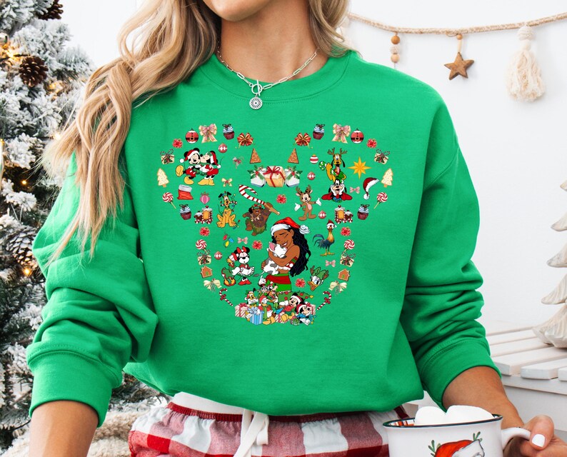 A woman wearing a green sweater with a large, colorful design of various Disney characters and holiday-themed elements.