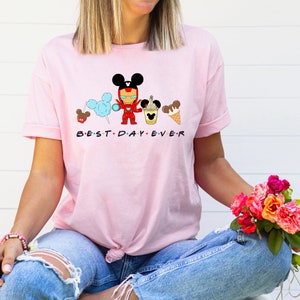 May include: Pink t-shirt with a graphic of Mickey Mouse, Iron Man, and other Disney characters. The text "BEST DAY EVER" is printed below the graphic.