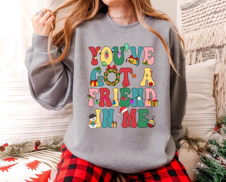 A woman wearing a gray sweatshirt with a colorful text design that says "YOU'VE GOT A FRIEND IN ME" printed on it.