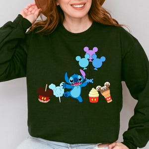 A woman wearing a black sweatshirt with a graphic design featuring a cartoon character and various Disney-themed items such as Mickey Mouse, a hot dog, and a cupcake.