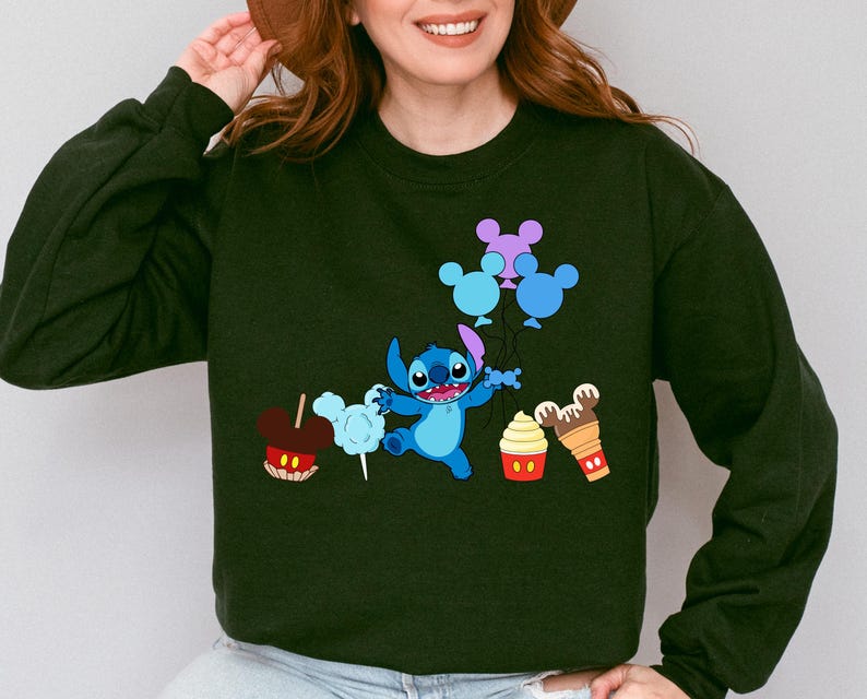 A woman wearing a black sweatshirt with a graphic design featuring a cartoon character and various Disney-themed items such as Mickey Mouse, a hot dog, and a cupcake.