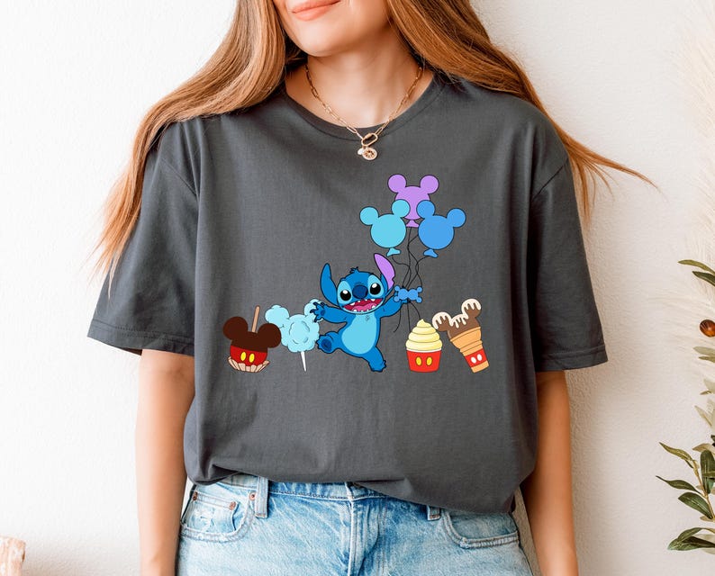 A woman wearing a gray t-shirt with a graphic design featuring a cartoon character surrounded by various Disney-themed items such as Mickey Mouse, cotton candy, and ice cream cones.