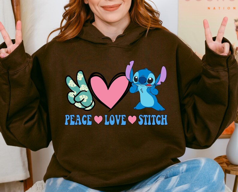 A woman wearing a brown hoodie with a graphic design featuring a peace sign and a heart, along with the text "PEACE LOVE STITCH".