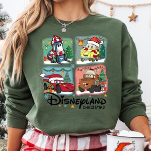 A person wearing a green sweatshirt with a collage of four Disney Cars characters from the movie "Disneyland Christmas" on it.