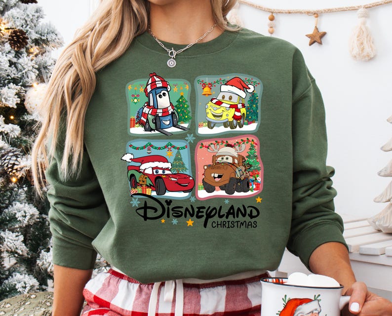 A person wearing a green sweatshirt with a collage of four Disney Cars characters from the movie "Disneyland Christmas" on it.