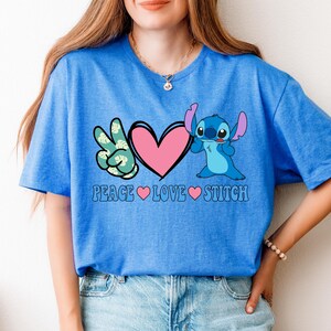 A woman wearing a blue t-shirt with a graphic design featuring a character from the animated series Lilo and Stitch, along with the text "Peace Love Stitch".