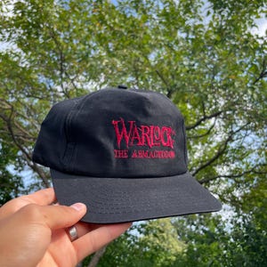 May include: Black baseball cap with red embroidered text that reads "Warlock The Armageddon".
