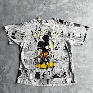 May include: White t-shirt featuring a large Mickey Mouse graphic with a comic strip design. Mickey is in his classic pose, wearing red shorts and yellow shoes. The shirt has a crew neck and short sleeves.