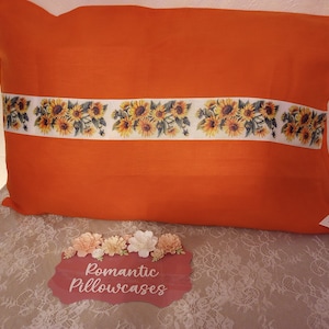 May include: Orange pillowcase with a white trim and a row of sunflower print. The pillowcase is on a lace tablecloth with a sign that reads "Romantic Pillowcases".