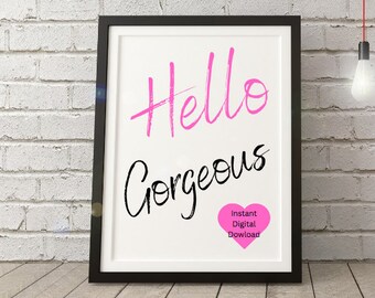 以下が含まれることがあります： ピンクと黒の筆文字で「Hello Gorgeous」と書かれた額装された印刷物。右下隅には、「インスタントデジタルダウンロード」というテキストが書かれたピンクのハートがあります。