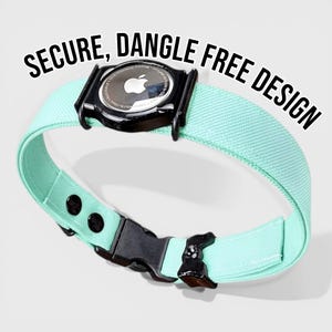 Puede incluir: Un collar de color verde azulado claro con una hebilla negra y un soporte negro para un Apple AirTag. El collar tiene el texto "SECURE, DANGLE FREE DESIGN" en negro. El collar está diseñado para sujetar de forma segura el AirTag.
