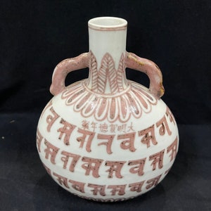 Peut inclure: Un vase en céramique blanche avec deux anses et un motif floral rose. Le vase est décoré de caractères chinois qui signifient "Bonne année".