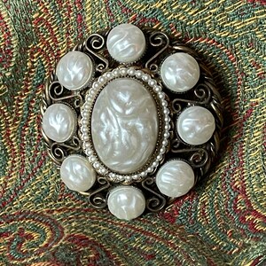 May include: A vintage brooch with a large oval white faux pearl surrounded by smaller white faux pearls and a gold-toned metal frame.