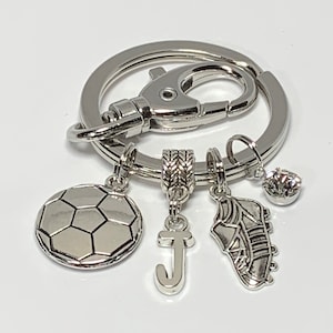 May include: Silver keychain with a soccer ball charm, a letter J charm, a soccer cleat charm, and a small rhinestone charm.