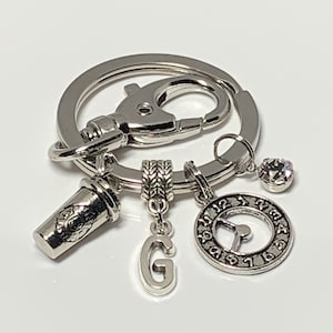 May include: Silver keychain with a coffee cup charm, a clock charm, a letter G charm, and a crystal charm.