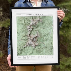 May include: A framed topographic map of Mount Washington in New Hampshire, USA. The map shows the mountain's terrain and surrounding area in detail. The title "Mount Washington" is printed at the top of the map. The map is printed on white paper and framed in a black frame.