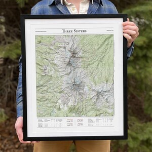 May include: A framed map of the Three Sisters Wilderness in the Cascade Mountains of Oregon. The map shows the trails, elevation, and other features of the area. The map is printed on white paper and has a black frame.