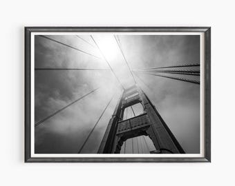 May include: A black and white photograph of the Golden Gate Bridge in San Francisco, California. The photo is taken from a low angle, looking up at the bridge's tower. The bridge is shrouded in fog, giving the image a mysterious and ethereal feel.