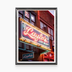May include: A neon sign for Layla's Honky Tonk, a bar in a brick building with a blue and green awning. The sign is lit up with red and yellow lights.