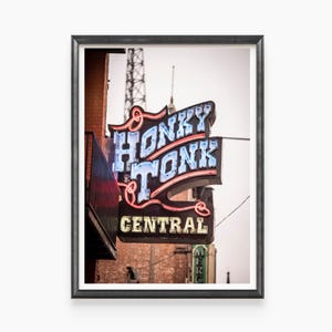 May include: A neon sign with the words "Honky Tonk Central" in red, blue, and yellow letters. The sign is attached to a brick building and has a vintage look.