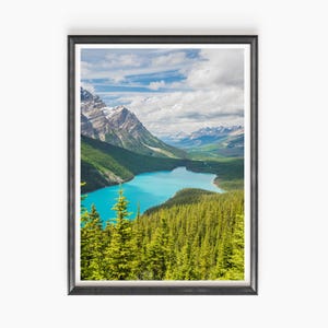 Peut inclure: Impression encadrée d'un paysage avec un lac turquoise entouré de forêts vertes et de montagnes aux sommets enneigés. Le ciel est un mélange de nuages bleus et blancs, créant une vue panoramique.