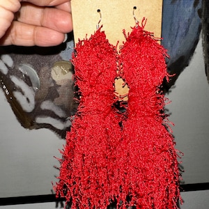 May include: A pair of red tassel earrings with silver hooks. The tassels are made of a soft, fluffy material and are about 7.5 cm long.