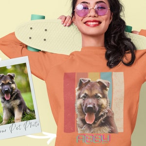 Peut inclure: Sweat-shirt orange avec une image rétro d'un chiot berger allemand avec le nom "Abby" imprimé en dessous. L'image est entourée de rayures verticales colorées.