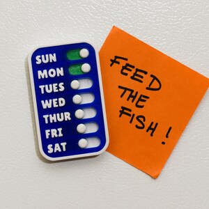 Compact magnetic checklist positioned alongside a vibrant post-it note reading "FEED THE FISH," offering a handy size reference for your organizational needs. Stay on top of your tasks with our sleek checklist design!