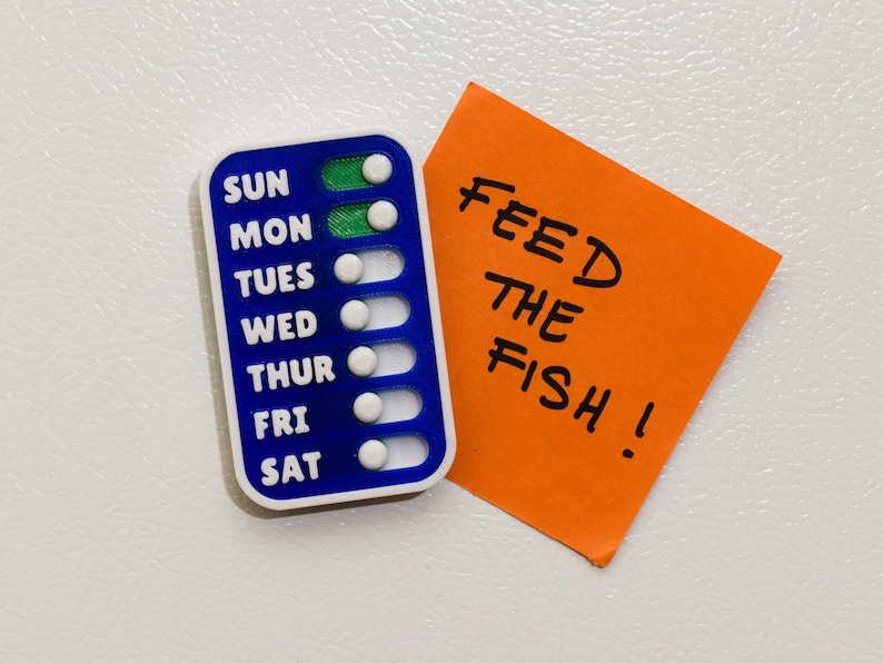 Compact magnetic checklist positioned alongside a vibrant post-it note reading "FEED THE FISH," offering a handy size reference for your organizational needs. Stay on top of your tasks with our sleek checklist design!