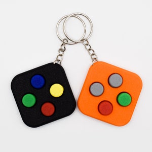 May include: A black and orange keychain with four buttons on each side. The buttons are different colours, including red, green, blue, yellow, and grey.