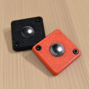 May include: Two square-shaped, textured, push buttons with a round, silver-coloured button in the centre. One button is black and the other is orange.