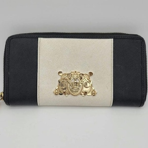May include: A black, cream, and gold wallet with a zip closure. The wallet has a cream central panel with black panels on either side. A gold emblem is centered on the cream panel.