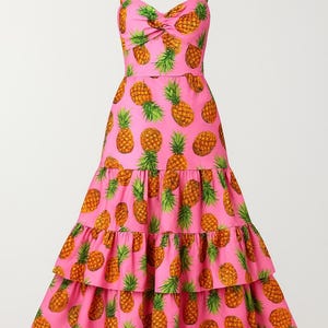 May include: A pink dress with a repeating pattern of pineapples. The dress has a sweetheart neckline, spaghetti straps, and a tiered skirt. The pineapples are yellow and orange with green tops.