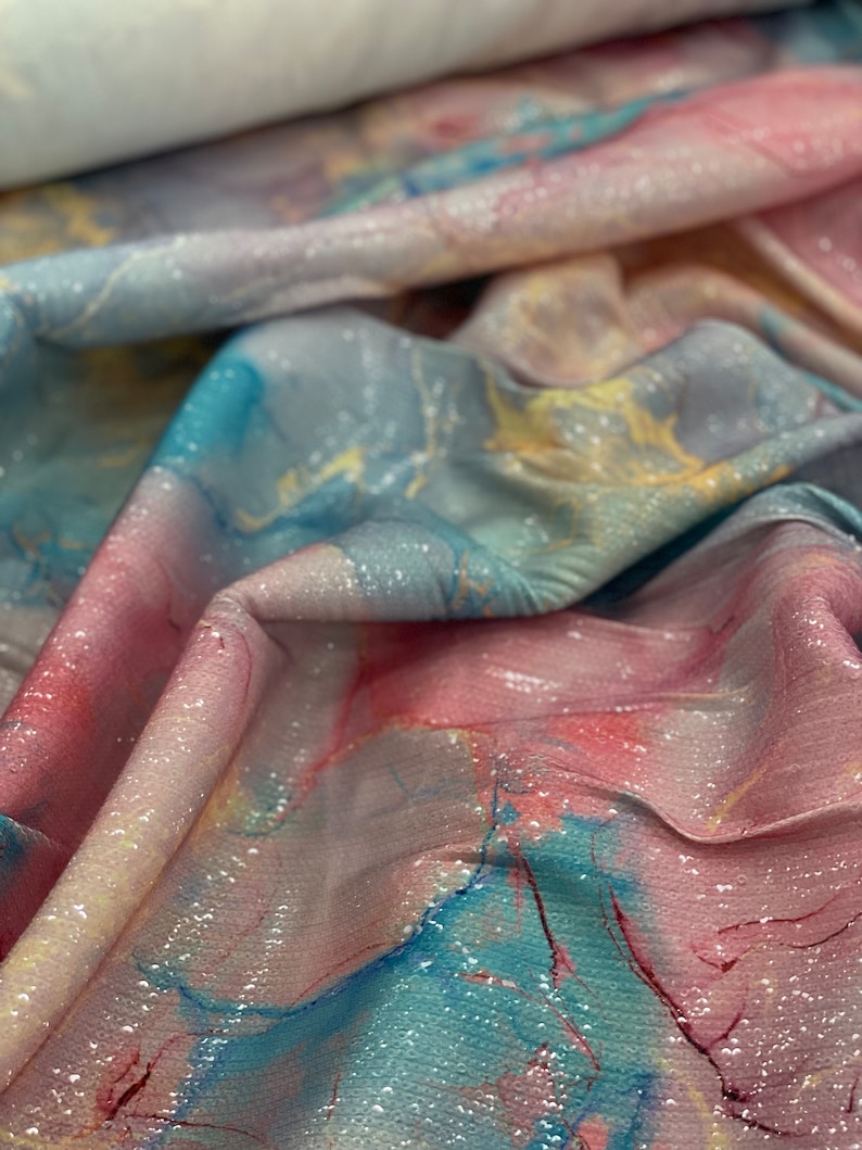 May include: Close-up of a pink, blue, and yellow fabric with a marble-like pattern and a glittery finish.