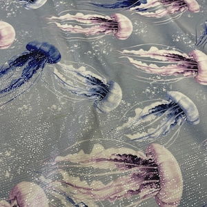 May include: A blue and white fabric with a repeating pattern of jellyfish. The jellyfish are a light purple and white colour with blue tentacles.