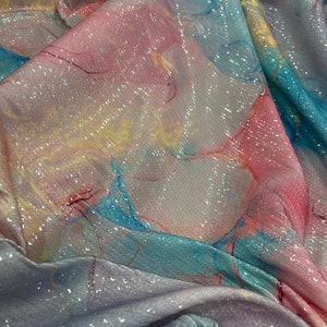 May include: A close-up of iridescent fabric with a marbled pattern in shades of pink, blue, and yellow. The fabric is covered in sequins that shimmer in the light.