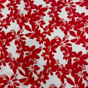 May include: White fabric with a repeating pattern of red floral shapes. The flowers have multiple petals and are scattered across the surface. The design is bold and eye-catching, suitable for various fabric applications.