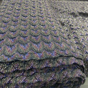 Puede incluir: Primer plano de una tela negra y azul con un patr&oacute;n texturizado e iridiscente. La tela est&aacute; doblada y enrollada, mostrando la textura y el brillo del material.