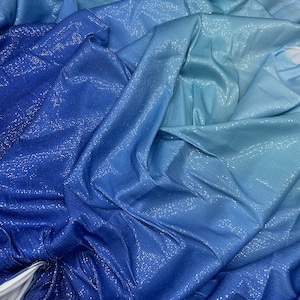 May include: A close-up of a fabric with a blue colour gradient, shifting from dark indigo to a light sky blue. The material has a subtle, shimmering texture, catching the light. The fabric is draped and folded, creating a dynamic visual effect.
