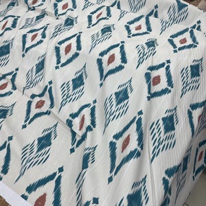 May include: White fabric with a teal and rust colored geometric pattern. The fabric has a subtle sheen and a soft texture.