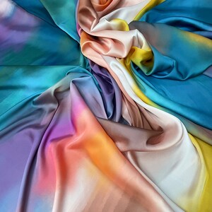 May include: A colorful fabric with a gradient pattern in shades of blue, purple, pink, orange, and yellow. The fabric is folded and draped, creating a soft and flowing texture.