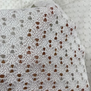 Puede incluir: Tela de crochet blanca con un patrón geométrico. La tela está hecha de un hilo fino y delicado y tiene una sensación suave y aireada.