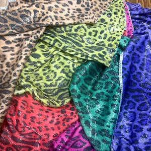 May include: A stack of six different leopard print fabrics with sequins. The fabrics are in the colours brown, green, red, pink, blue, and purple.
