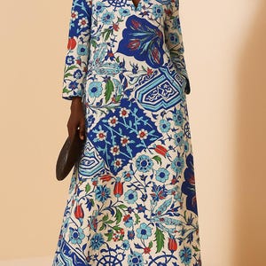 Puede incluir: Vestido largo y fluido con cuello en V y mangas largas. El vestido presenta un vibrante estampado floral en tonos azules, blancos, rojos y verdes. El diseño incluye flores estilizadas y formas geométricas. El vestido se lleva con sandalias.