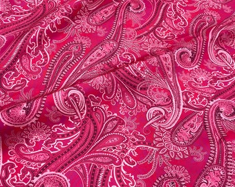 Puede incluir: Primer plano de una tela con un estampado de cachemira en tonos rojos y rosas. El diseño presenta intrincados motivos arremolinados con acentos blancos. La tela está drapeada, creando sombras y reflejos que enfatizan la complejidad del patrón.