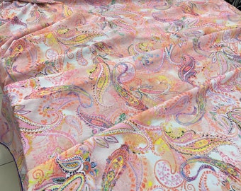 Puede incluir: Una tela de estampado paisley rosa y blanco con acentos amarillos, azules y morados. La tela es suave y fluida, lo que la hace ideal para una variedad de proyectos de costura.